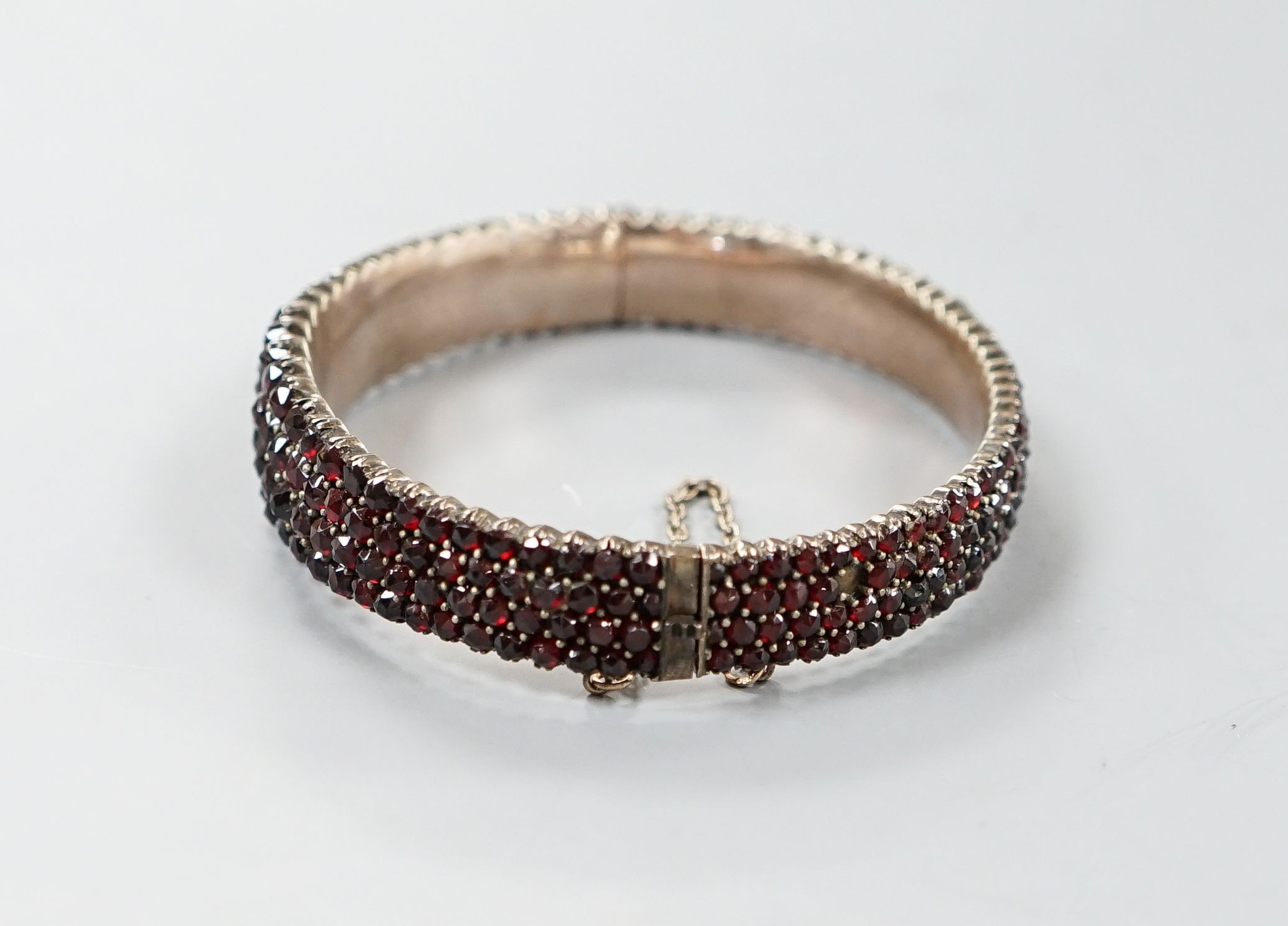 A late Victorian gilt white metal and garnet encrusted hinged bangle (stone missing).
